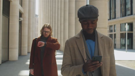 Black-Businessman-Walking-on-Street-and-Using-Smartphone